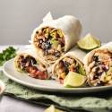 A plate of fresh and flavorful Fish Burritos, packed with black beans, corn, avocado, cabbage slaw, and juicy seasoned fish, wrapped in soft tortillas and served with lime wedges. 